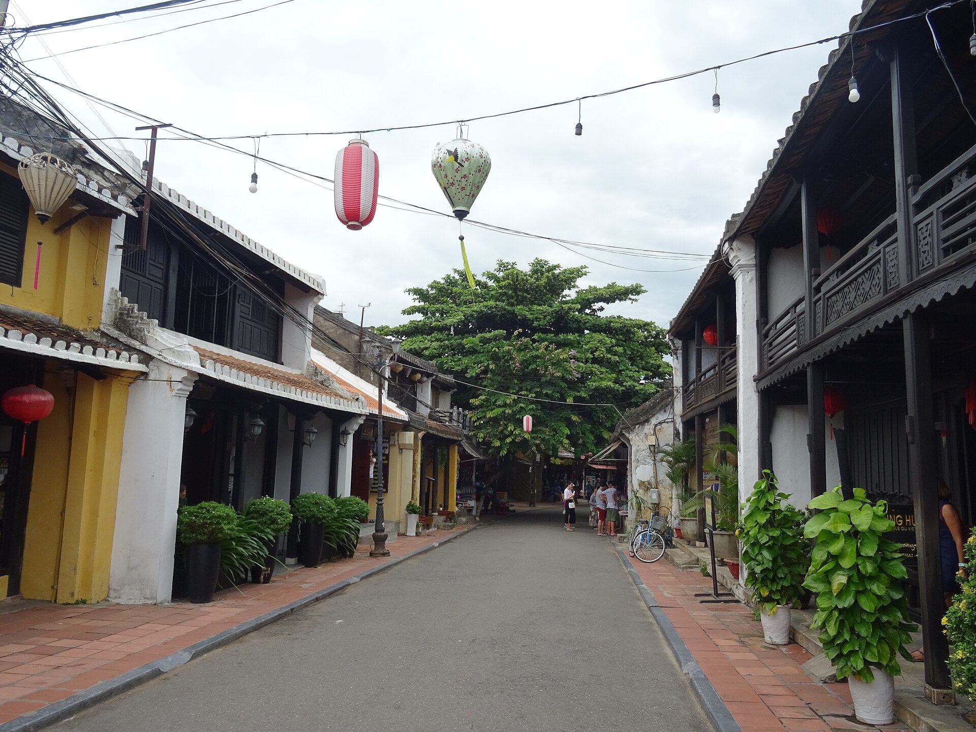 A Hội An street lined with yellow-walled buildings, timber upper storeys and hanging lanterns.