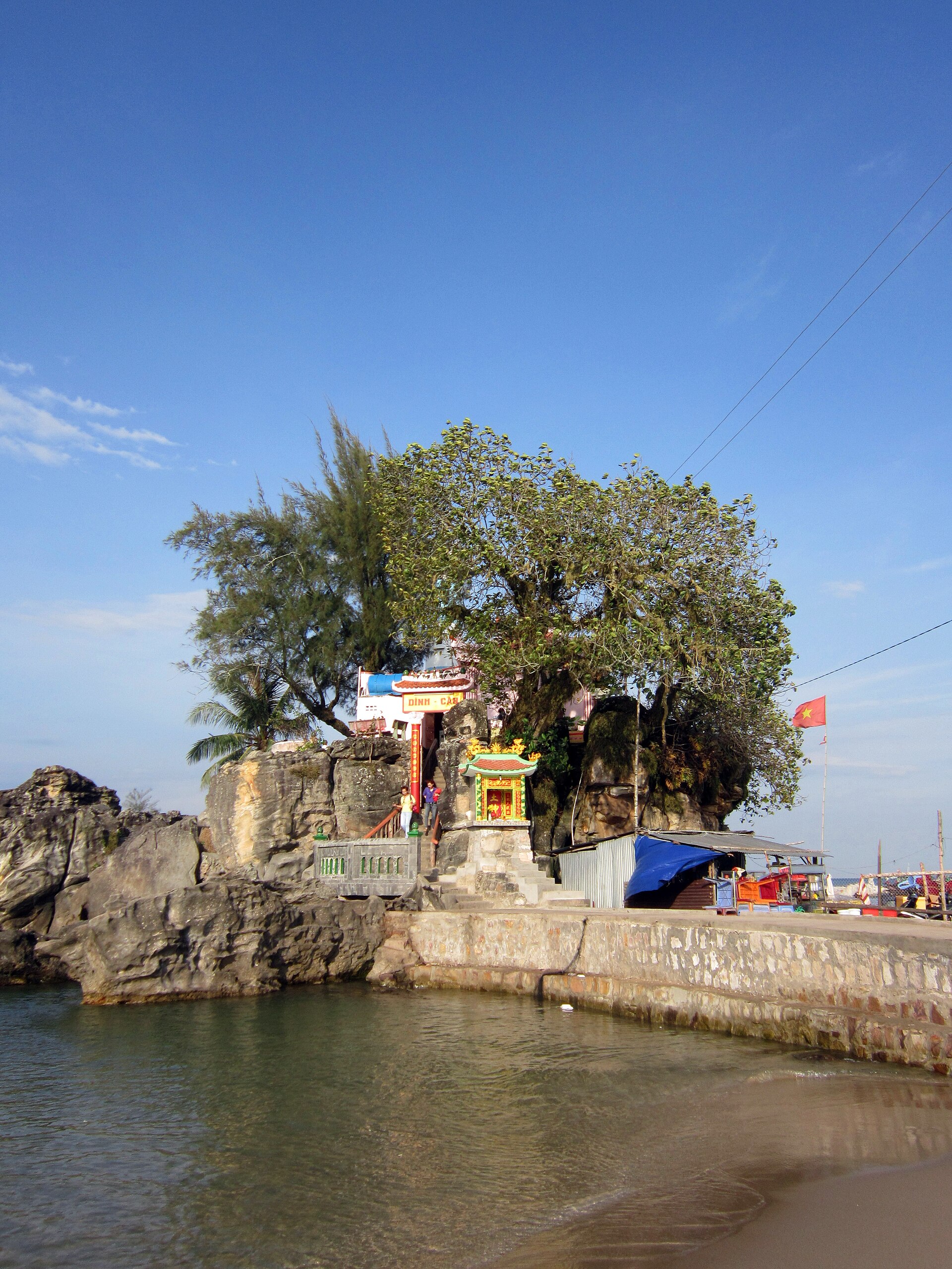 Dinh Cậu shrine and trees stand on a rocky promontory beside the sea at Dương Đông.