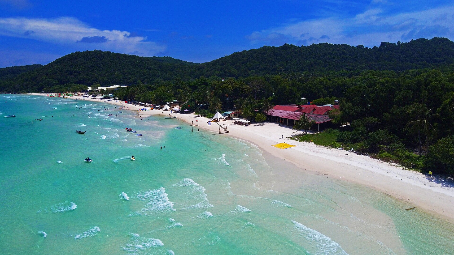 An aerial view of Bãi Sao on Phú Quốc, with turquoise water, a curved sandy shore and forested hills.